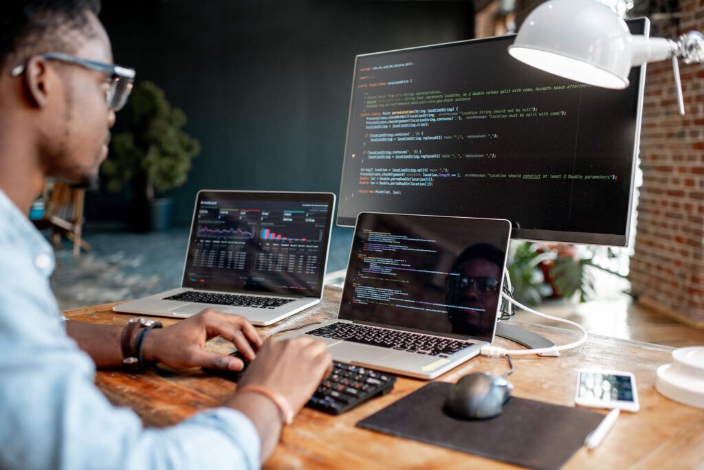 man designing a website with 2 laptops and 1 other screen