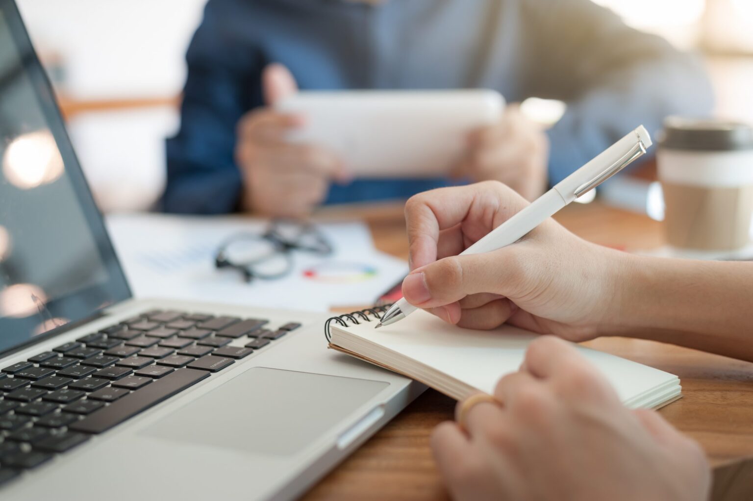 Young worker writing on notebook while working with colleague
