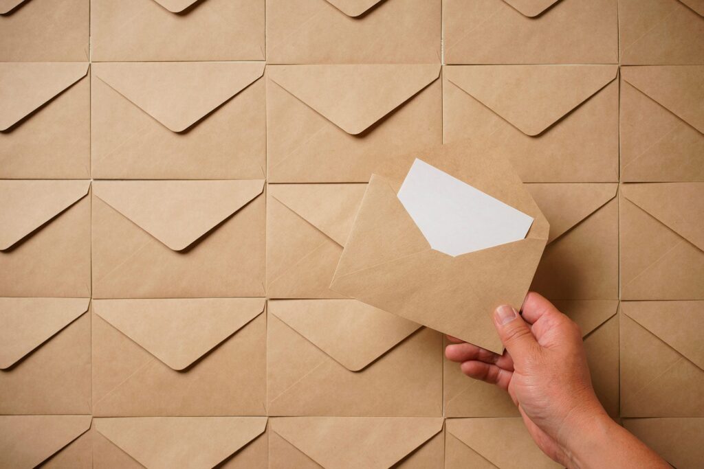 hand holding a brown envelope with white card inside in front of a wall of brown envelopes